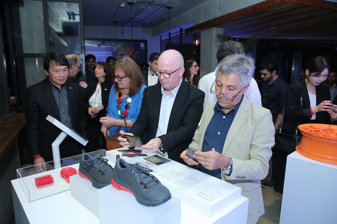 People looking at a display with two 3D-printed Under Armour sneakers.