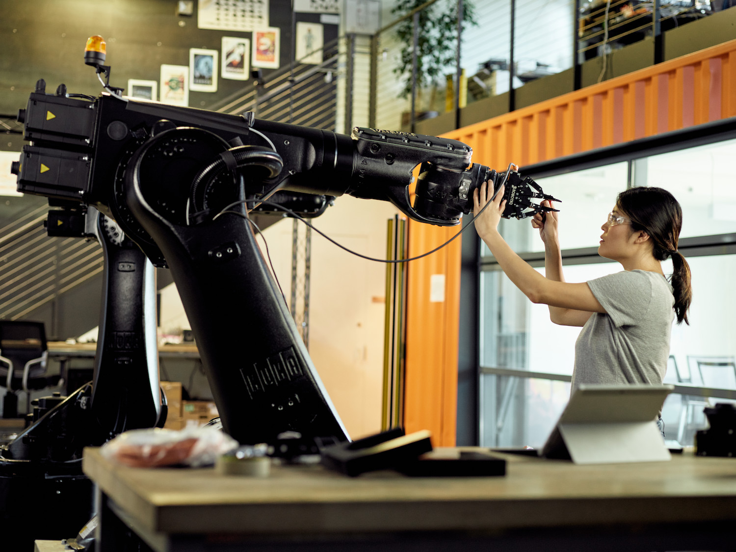 A woman in a lab space touching a large robotic arm.