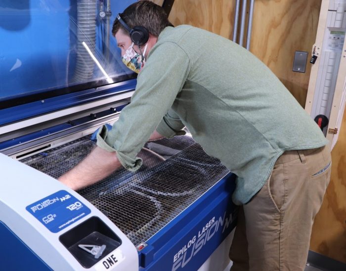 A workshop member at the Bman uses a laser cutter to cut PET material for face shields. 