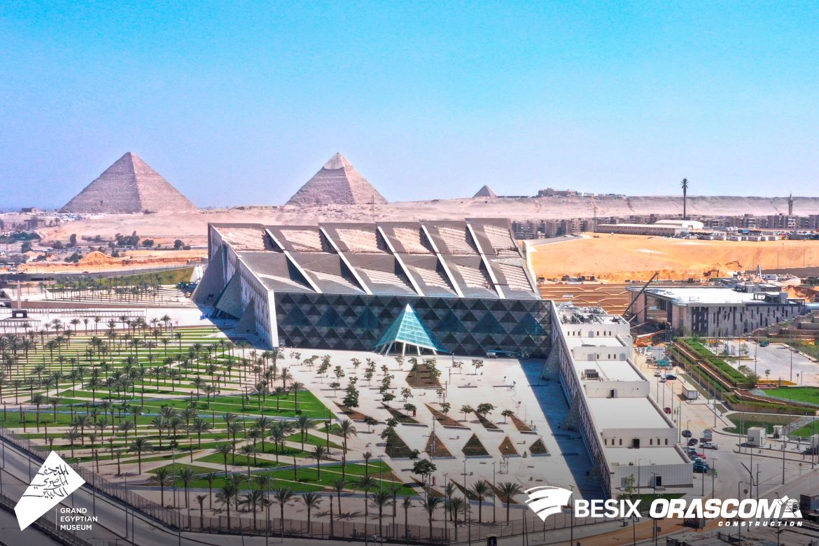 Modern builing alongside greenery, desert terrain and the pyramids