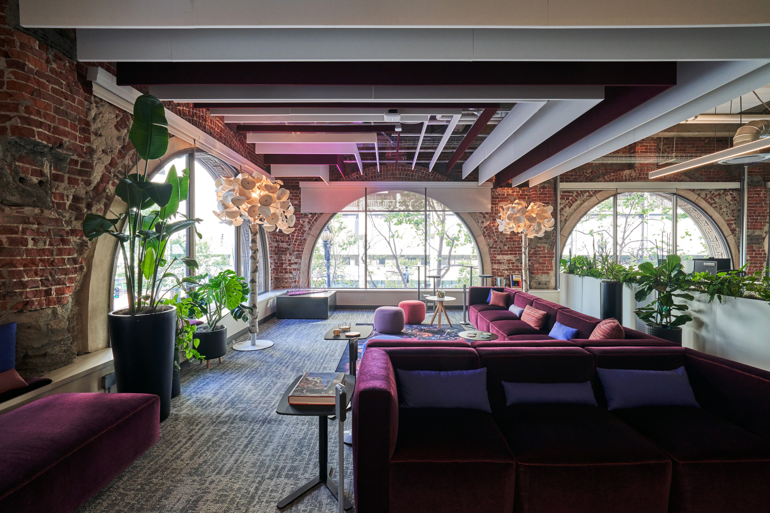 Hybrid work space with large arched windows, couches and houseplants.