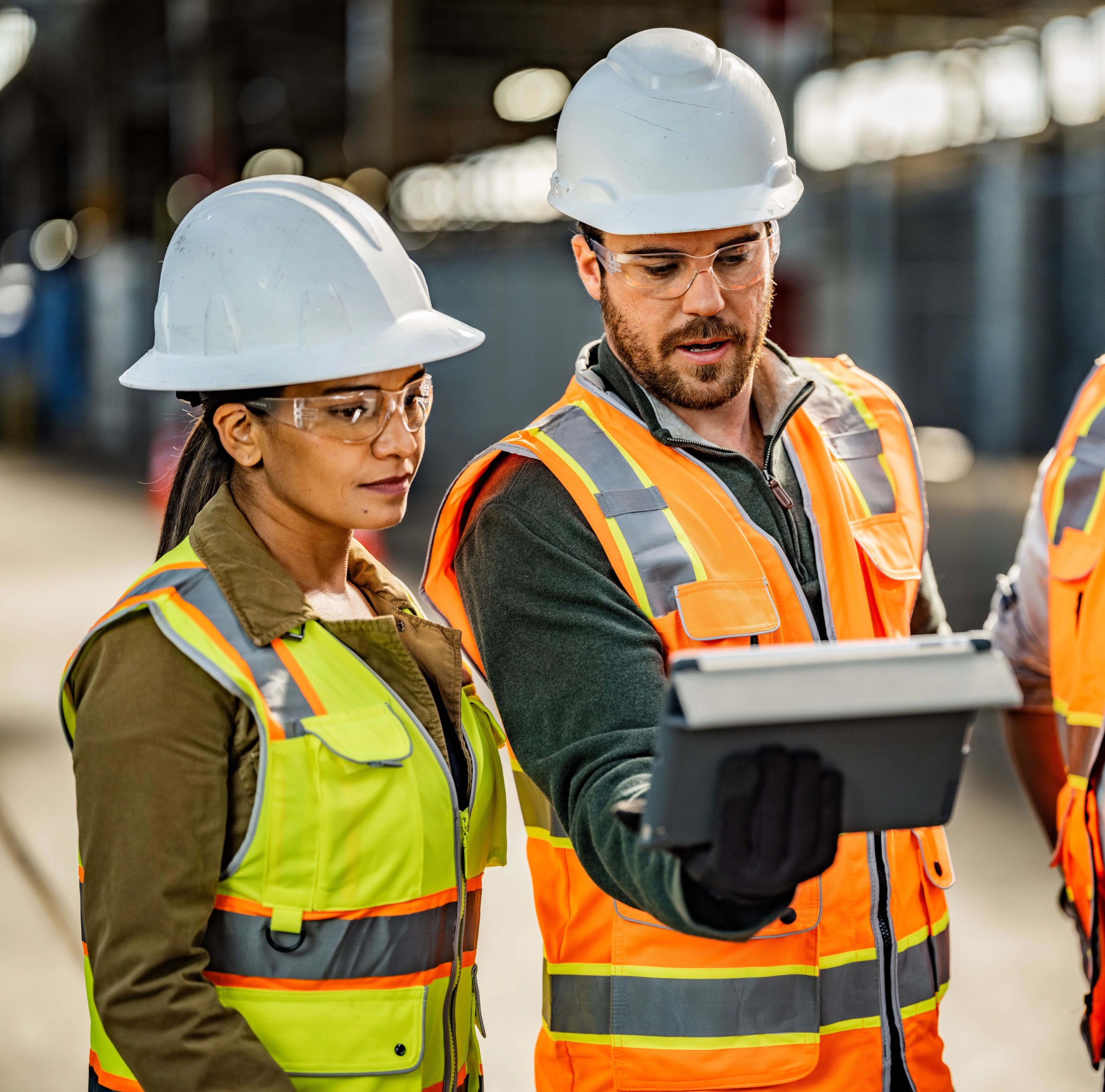 2 people with helmets and construction vests look at a screen