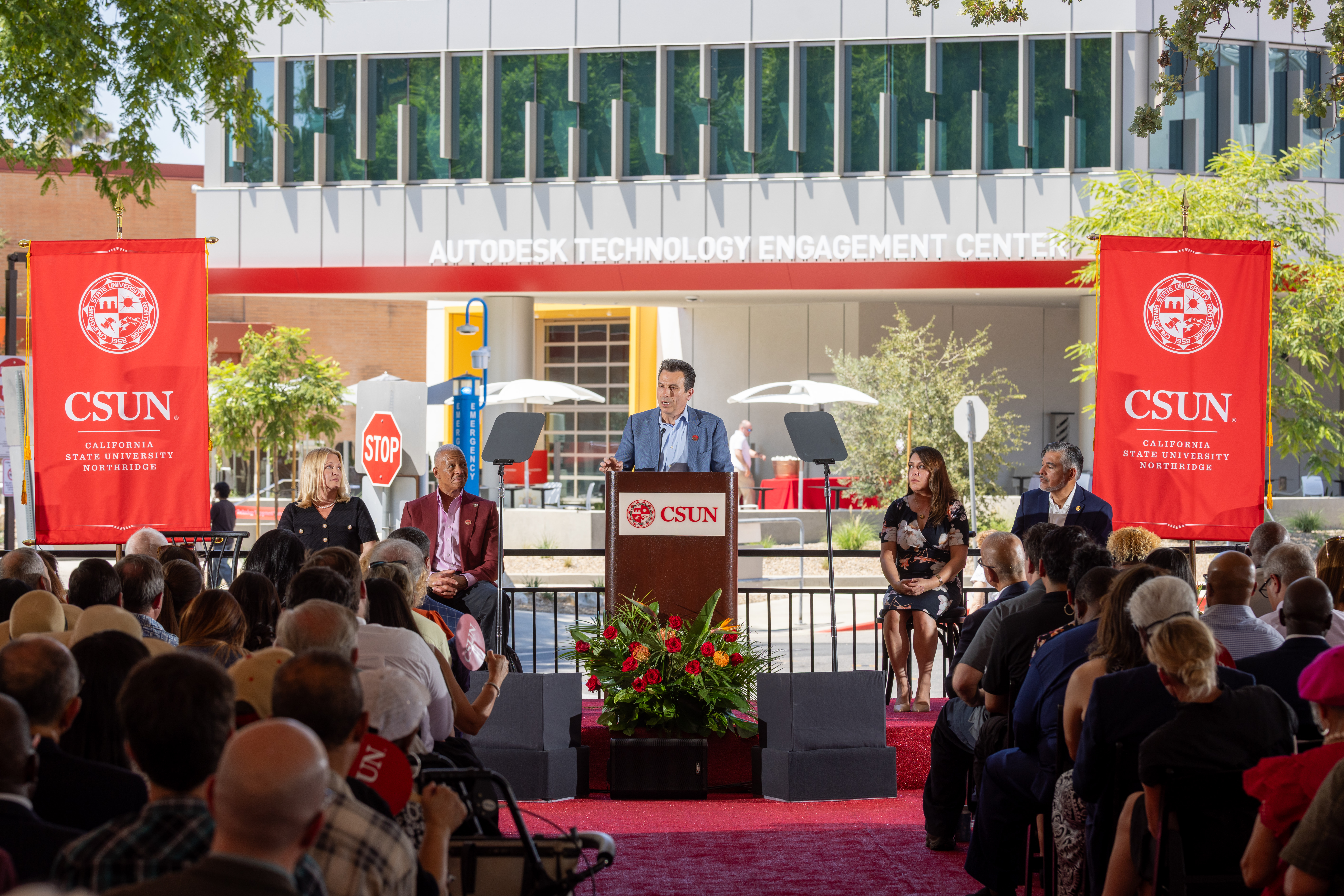 Andrew Anagnost speaking at a podium in front of a group of people outside the Autodesk Technology Engagement Center